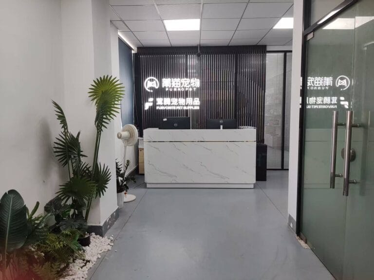 Reception area of StridePaw’s pet products office with a white marble front desk, indoor plants, and illuminated company logo on the back wall.