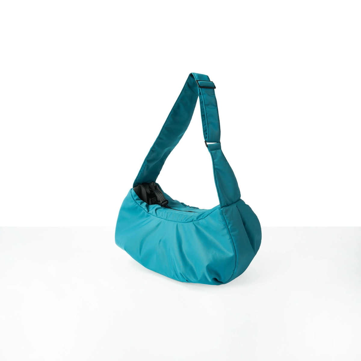 Alternate angled view of a StridePaw teal pet sling bag featuring a wide padded strap, open-top design, and visible built-in safety tether for small pets