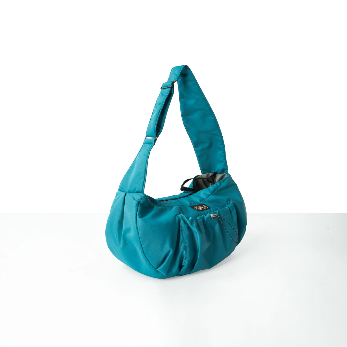 Angled view of a StridePaw teal pet sling carrier with cushioned body, open-top seat for easy pet access, and front pocket for everyday essentials